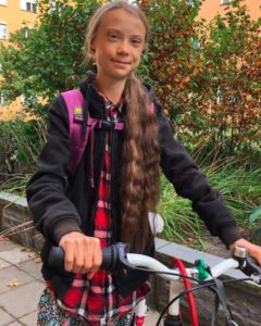 Greta Thunberg (an autistic cylist) on bicycle smiling at camera